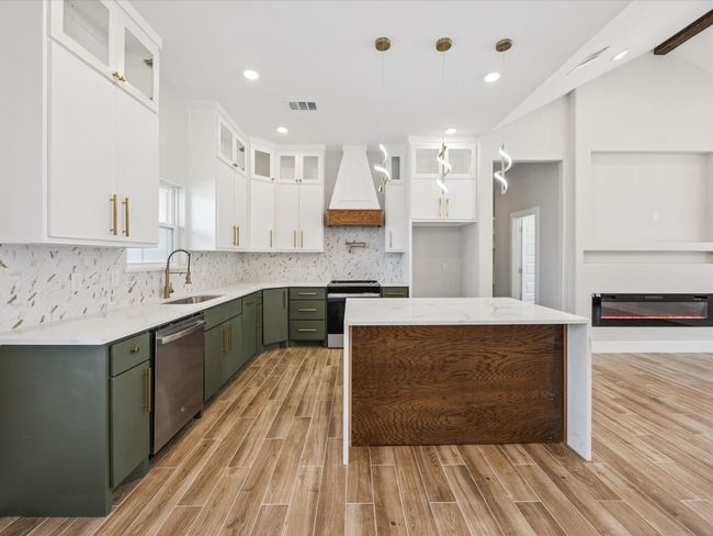 Kitchen featuring appliances with stainless steel finishes, premium range hood, light wood-style floors, green cabinetry, and white cabinetry | Image 12