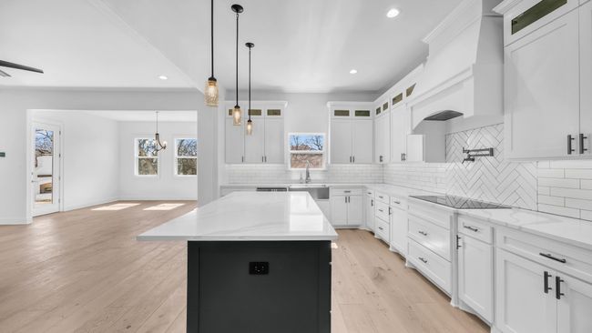 Kitchen with a kitchen island, custom range hood, decorative backsplash, light wood-style flooring, and black electric cooktop | Image 17