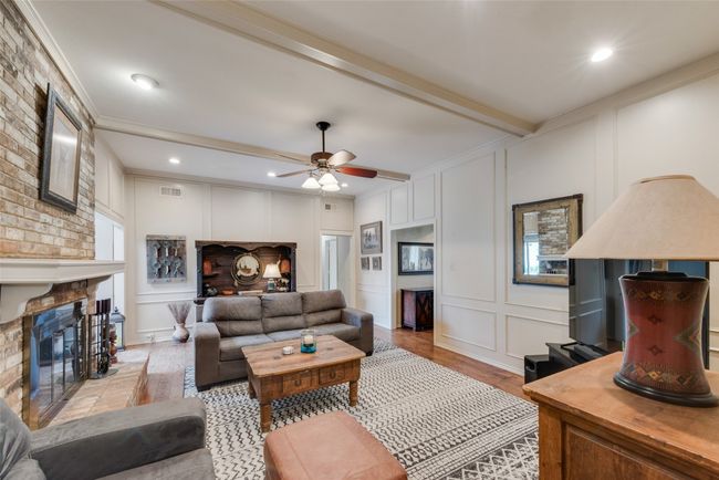 Living room with a decorative wall, a brick fireplace, light wood-type flooring, ornamental molding, and a ceiling fan | Image 9
