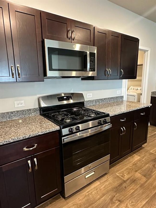 Kitchen with stainless steel appliances, separate washer and dryer, light wood-type flooring, light stone countertops, and dark brown cabinets | Image 4