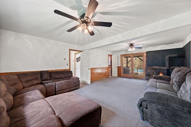 Living area with a wood stove, a wainscoted wall, ceiling fan, and light colored carpet | Image 24
