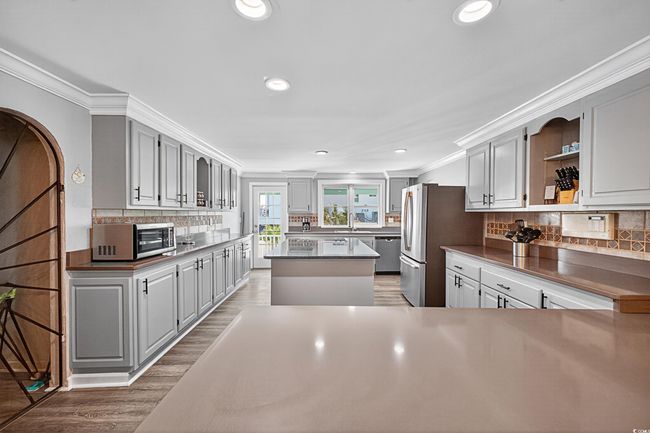 Kitchen featuring stainless steel appliances, open shelves, crown molding, decorative backsplash, and light wood-style floors | Image 34