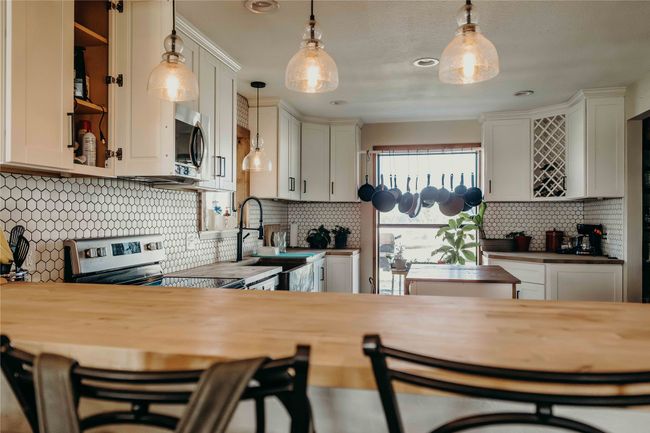 Kitchen with stainless steel appliances, tasteful backsplash, decorative light fixtures, butcher block countertops, and a kitchen breakfast bar | Image 9