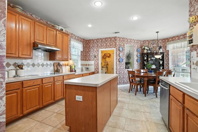 Kitchen with under cabinet range hood, wallpapered walls, brown cabinetry, black electric stovetop, and stainless steel dishwasher | Image 12
