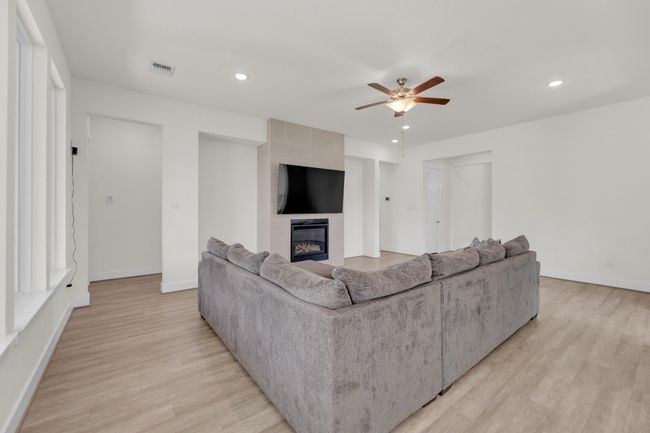 Living area featuring a large fireplace, baseboards, light wood-style flooring, ceiling fan, and recessed lighting | Image 7