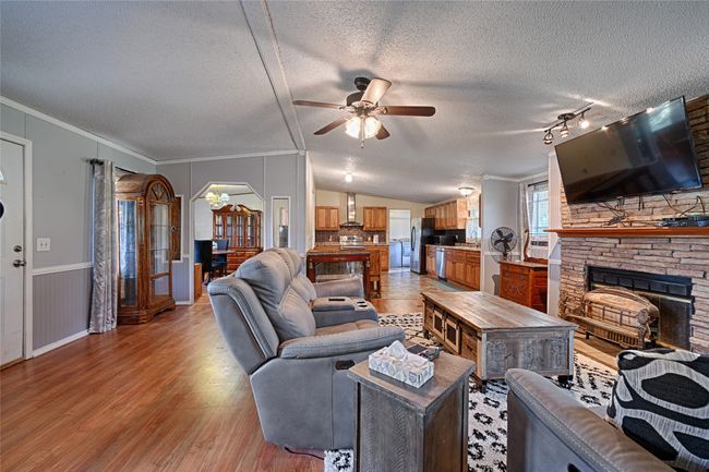 Living area with a textured ceiling, a stone fireplace, crown molding, light wood-style floors, and ceiling fan | Image 9