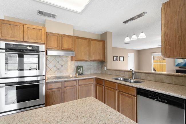 Kitchen with stainless steel appliances, a sink, backsplash, under cabinet range hood, and hanging light fixtures. | Image 20