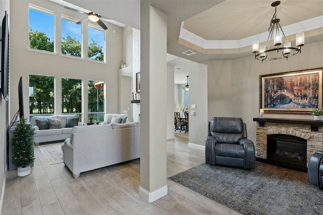 Living area with ceiling fan, dining or living area with a stone fireplace, ceramic tile wood-type flooring, ornamental molding, and a chandelier | Image 6