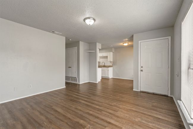 Unfurnished living room with dark wood-style flooring, baseboards, a textured ceiling, and a sink | Image 6