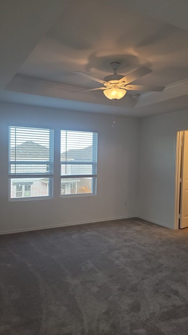 Unfurnished room featuring a ceiling fan, dark carpet, a raised ceiling, and baseboards | Image 9