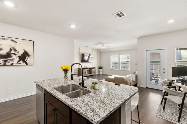 Kitchen with stainless steel dishwasher, a sink, dark wood finished floors, visible vents, and an island with sink | Image 7