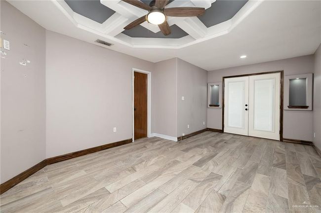 Unfurnished bedroom featuring beamed ceiling, french doors, ceiling fan, light hardwood / wood-style flooring, and coffered ceiling | Image 8