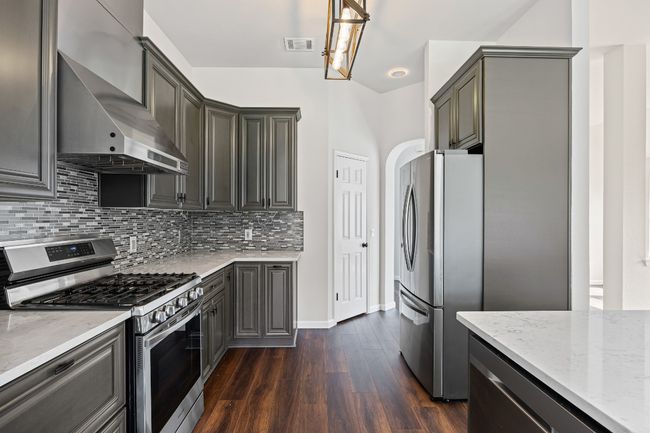 Kitchen featuring appliances with stainless steel finishes, wall chimney range hood, light stone counters, dark wood-style floors, and decorative backsplash | Image 8