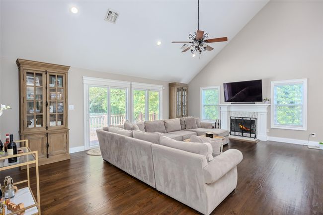 Living area featuring high vaulted ceiling, ceiling fan, a lit fireplace, dark wood-type flooring, and recessed lighting | Image 11