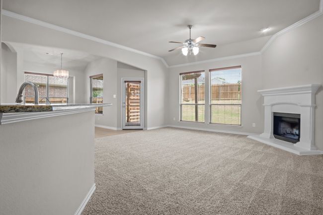 Unfurnished living room featuring ornamental molding, baseboards, light colored carpet, a fireplace with raised hearth, and ceiling fan with notable chandelier | Image 16