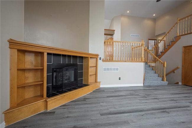 Unfurnished living room featuring wood finished floors, a tiled fireplace, stairs, baseboards, and a towering ceiling | Image 8