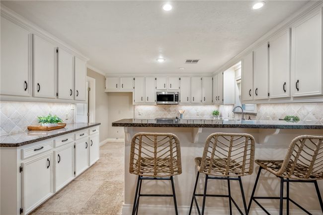 Kitchen with stainless steel microwave, backsplash, visible vents, and white cabinetry | Image 15