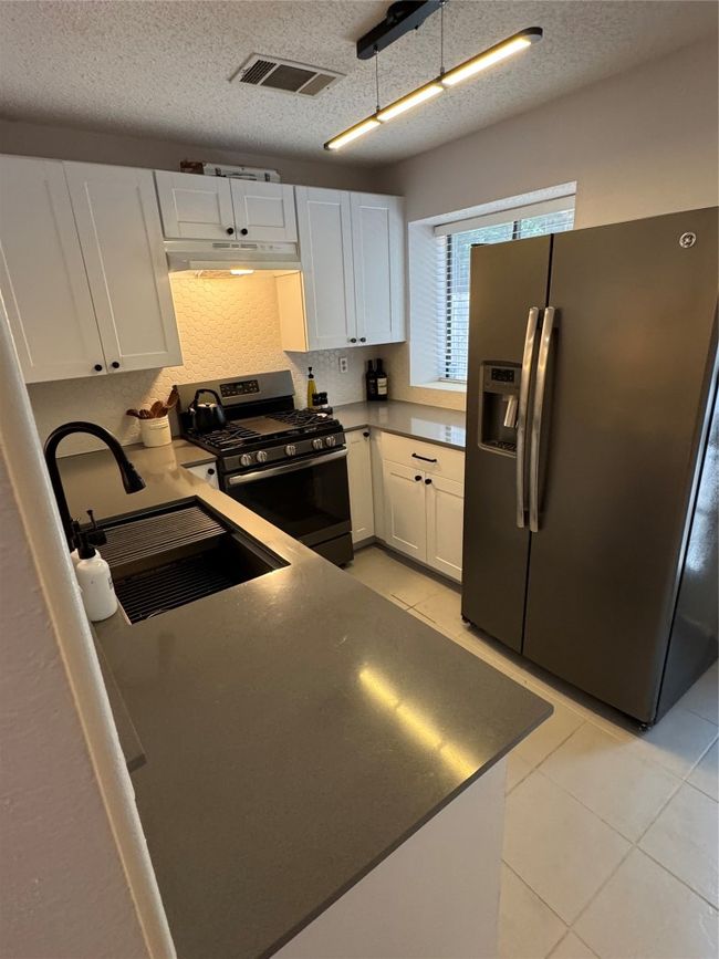 Kitchen featuring fridge, stove, extractor fan, white cabinets, and a textured ceiling | Image 7
