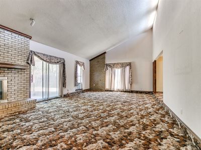 Unfurnished living room with high vaulted ceiling, a textured ceiling, a fireplace, and carpet flooring | Image 3