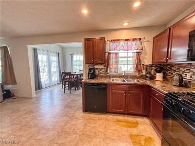 Kitchen featuring black appliances, backsplash, sink, a window, and a view of the morning room | Image 3