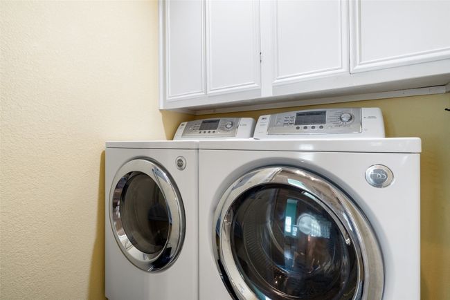 Clothes washing area featuring separate washer and dryer, cabinet space, and a textured wall | Image 31