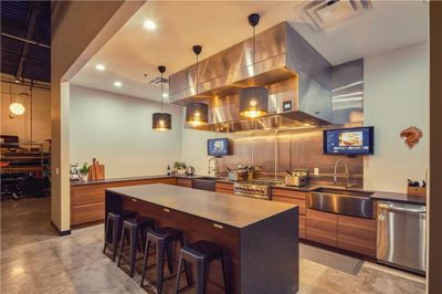 Kitchen featuring appliances with stainless steel finishes, a kitchen island, hanging light fixtures, a kitchen breakfast bar, and sink | Image 1