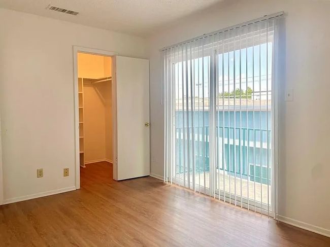 Unfurnished bedroom with a spacious closet, wood finished floors, and access to exterior | Image 4