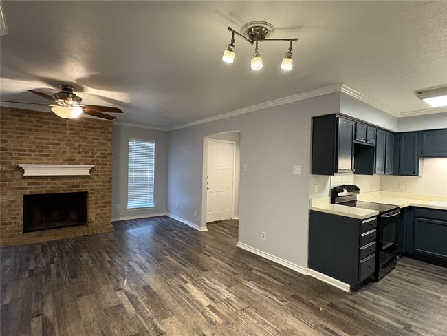 Kitchen with light countertops, electric range, dark wood-style floors, a brick fireplace, and a ceiling fan | Image 6