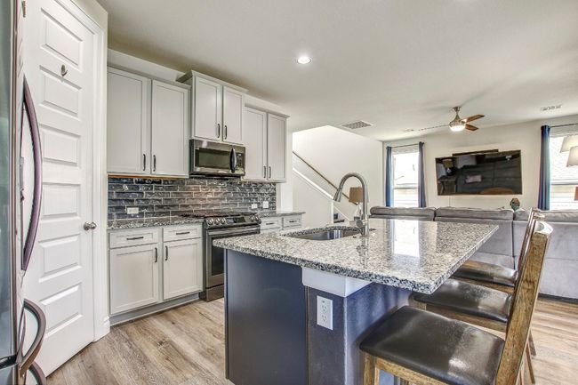 Kitchen featuring stainless steel appliances, open floor plan, light stone countertops, a kitchen breakfast bar, and backsplash | Image 11