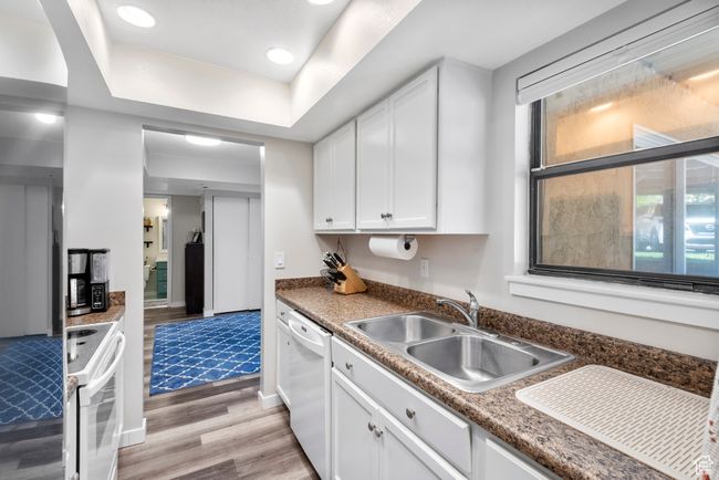 Kitchen featuring white appliances, light wood-type flooring, white cabinets, a tray ceiling, and recessed lighting | Image 15