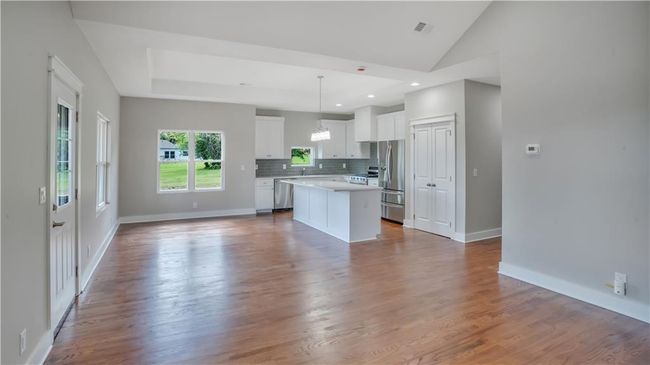 Kitchen with appliances with stainless steel finishes, a center island, white cabinets, decorative backsplash, and light countertops | Image 8