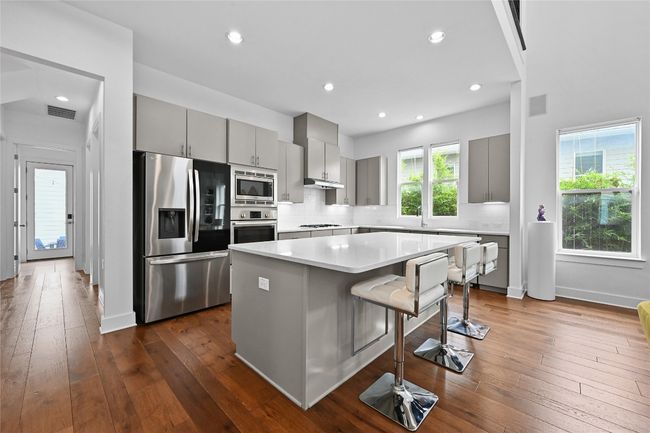 Kitchen featuring appliances with stainless steel finishes, gray cabinetry, a kitchen island, a kitchen breakfast bar, and light countertops | Image 8