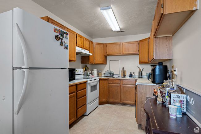 Kitchen featuring white appliances, under cabinet range hood, brown cabinetry, and light countertops | Image 37