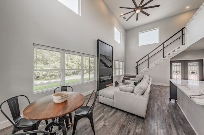 Living room with baseboards, a high ceiling, dark wood-style floors, ceiling fan, and stairway | Image 22