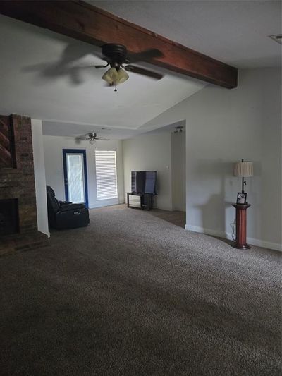 Unfurnished living room featuring ceiling fan, beam ceiling, carpet, and a brick fireplace | Image 3