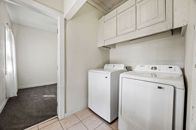 Washroom with light tile patterned floors, light colored carpet, baseboards, washer and dryer, and cabinet space | Image 16