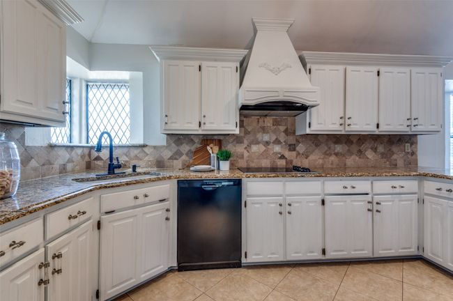 Kitchen featuring light tile patterned floors, a sink, white cabinets, custom exhaust hood, and black appliances | Image 16