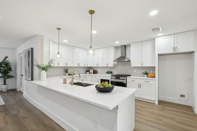 Kitchen with a sink, a peninsula, stainless steel gas range oven, wall chimney range hood, and visible vents | Image 5