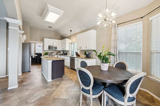 Kitchen featuring stainless steel appliances, a chandelier, lofted ceiling, a large center island, and white cabinets | Image 12