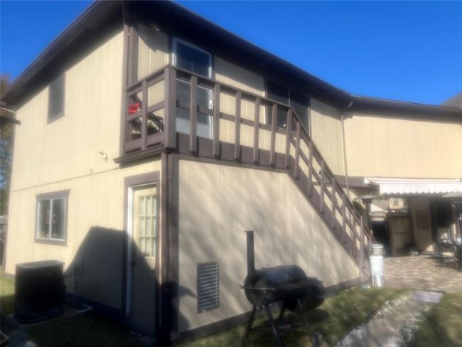 This photo shows a two-story house with beige siding and brown trim. It features an external staircase leading to an upper deck. The yard includes a grill and patio area. | Image 14