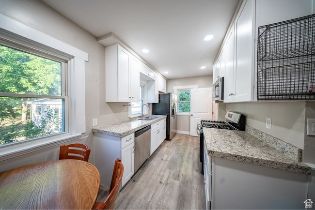 Kitchen featuring stainless steel appliances, light wood finished floors, white cabinetry, recessed lighting, and light stone counters | Image 12