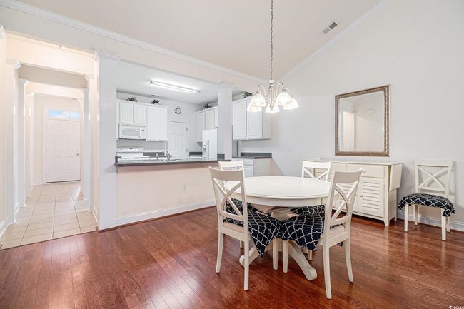 Dining area with vaulted ceiling, wood finished floors, baseboards, crown molding, and a chandelier | Image 13