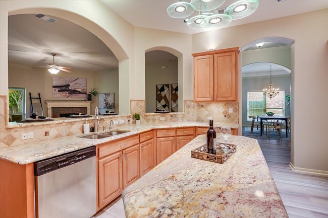 Kitchen with stainless steel dishwasher, a chandelier, light stone counters, backsplash, and light wood-type flooring | Image 4