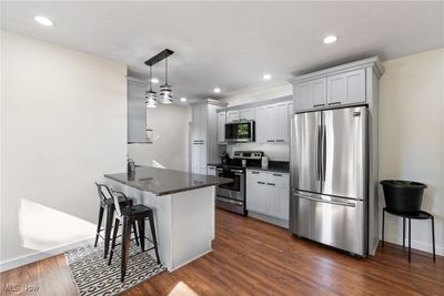 Kitchen featuring dark stone countertops, dark hardwood / wood-style flooring, kitchen peninsula, a breakfast bar, and appliances with stainless steel finishes | Image 3