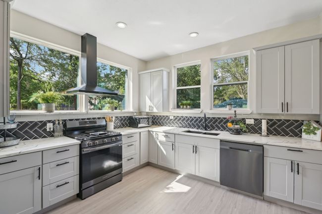 Kitchen with appliances with stainless steel finishes, wall chimney exhaust hood, decorative backsplash, a sink, and light stone countertops | Image 12