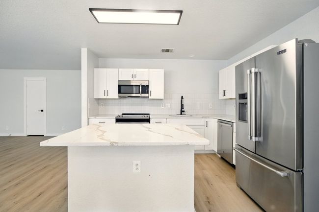 Kitchen with stainless steel appliances, decorative herringbone backsplash, and beautiful gold quartz countertops | Image 5