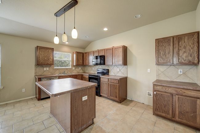 Kitchen featuring brown cabinets, black appliances, a center island, tasteful backsplash, and decorative light fixtures | Image 10