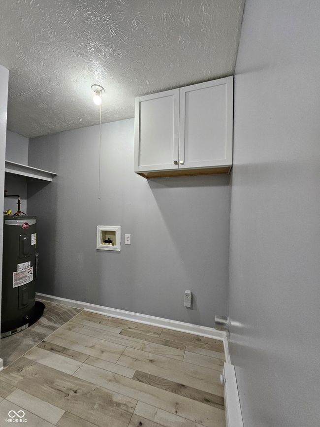 laundry room featuring cabinet space, water heater, washer hookup, light wood-style flooring, and a textured ceiling | Image 4