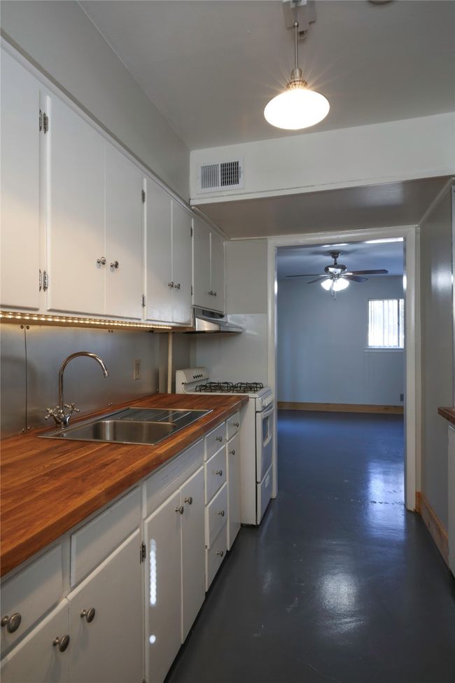 Kitchen with wood counters, white range with gas stovetop, under cabinet range hood, a ceiling fan, and white cabinetry | Image 11