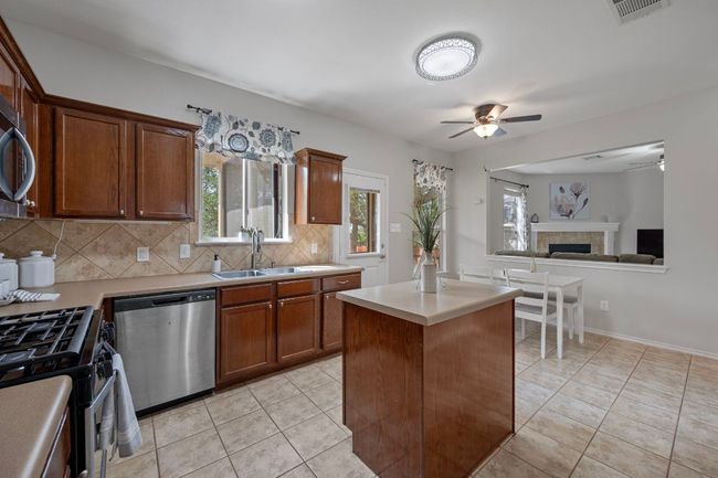Kitchen with stainless steel appliances, a ceiling fan, decorative backsplash, light countertops, and a sink | Image 12